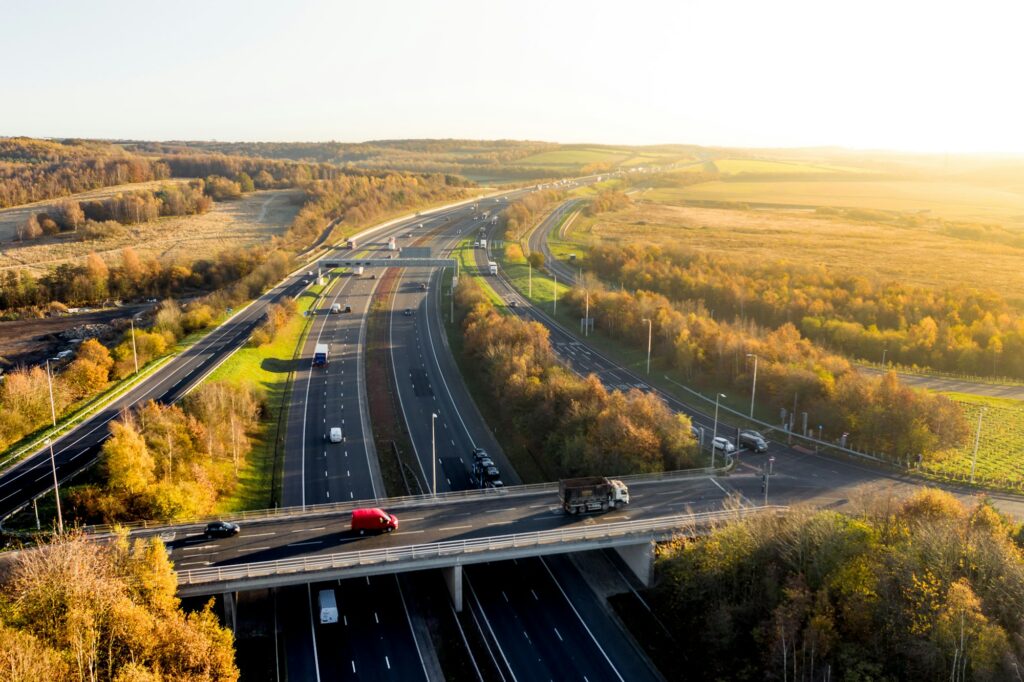 Aerial view of a busy motorway and over bridge running through woodland countryside at sunset